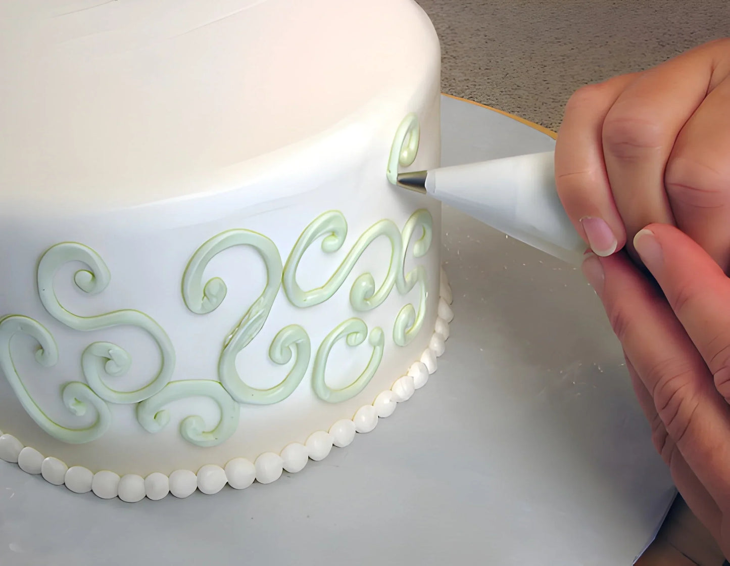 Cake piping bag with nozzle, decorating a cake edge with light green swirls