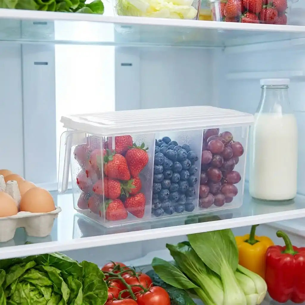 Clear divided refrigerator organizer box filled with berries and grapes on a shelf.