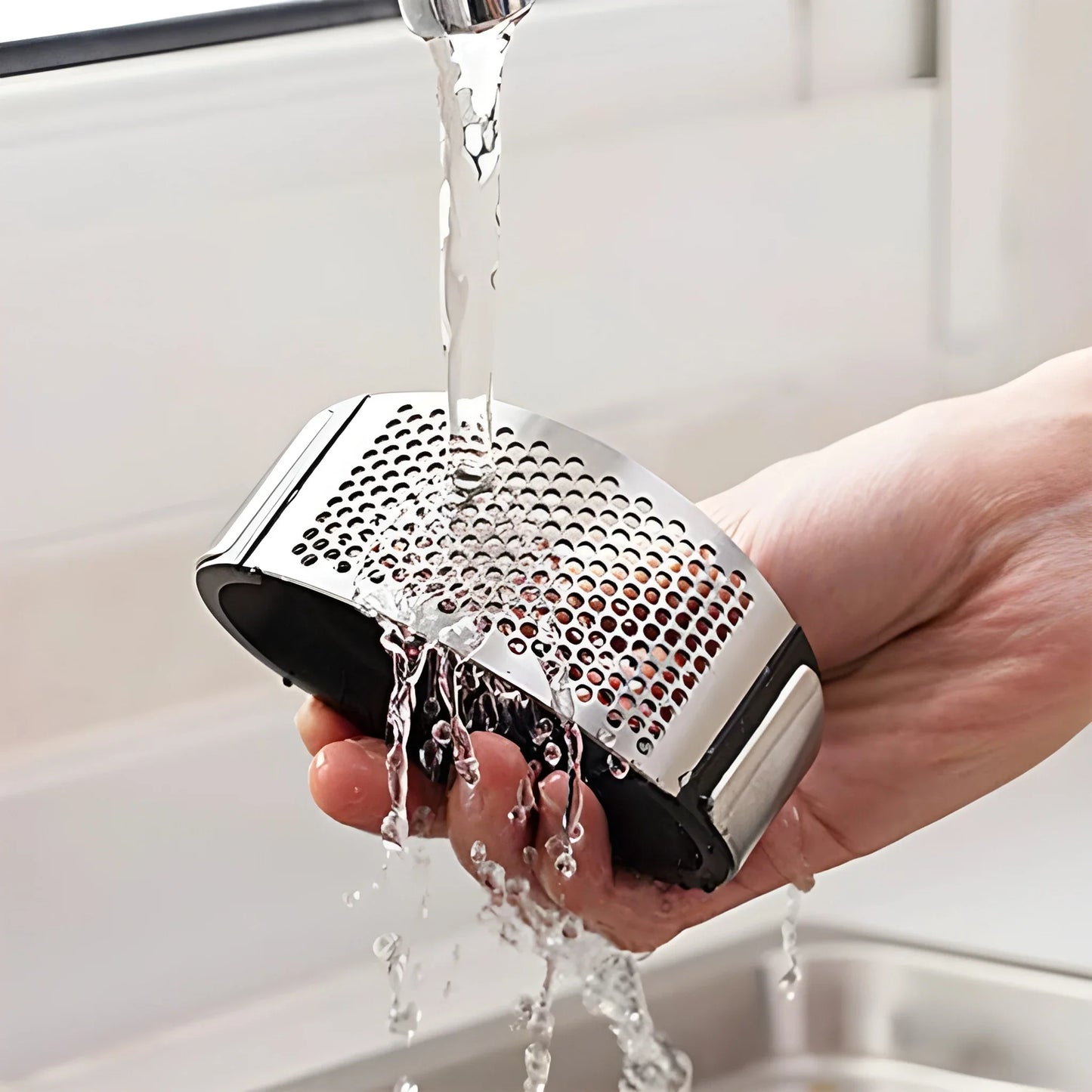 Stainless steel rocking garlic press with perforated crusher, held under running water