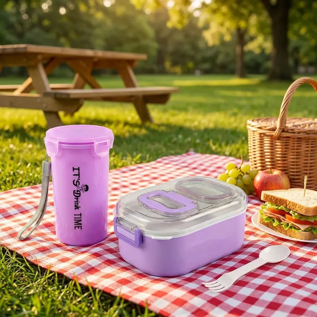 Lavender lunch box set with clear lid, cutlery, and tall snack cup on grass picnic