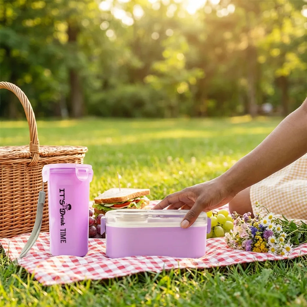 Lavender lunch box with clear lid and cutlery beside a tall snack cup