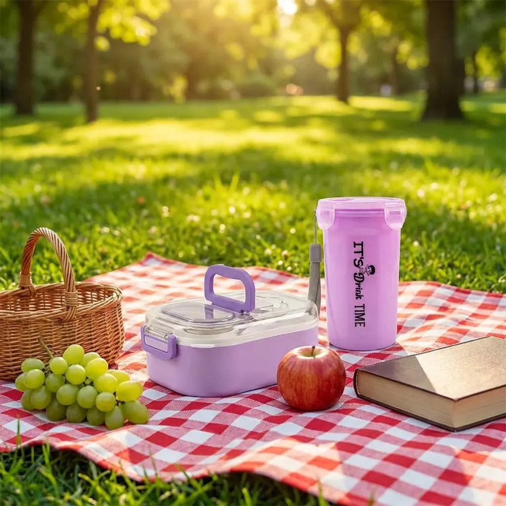 Lavender lunch box with cutlery and clear lid, plus tall snack cup on picnic table