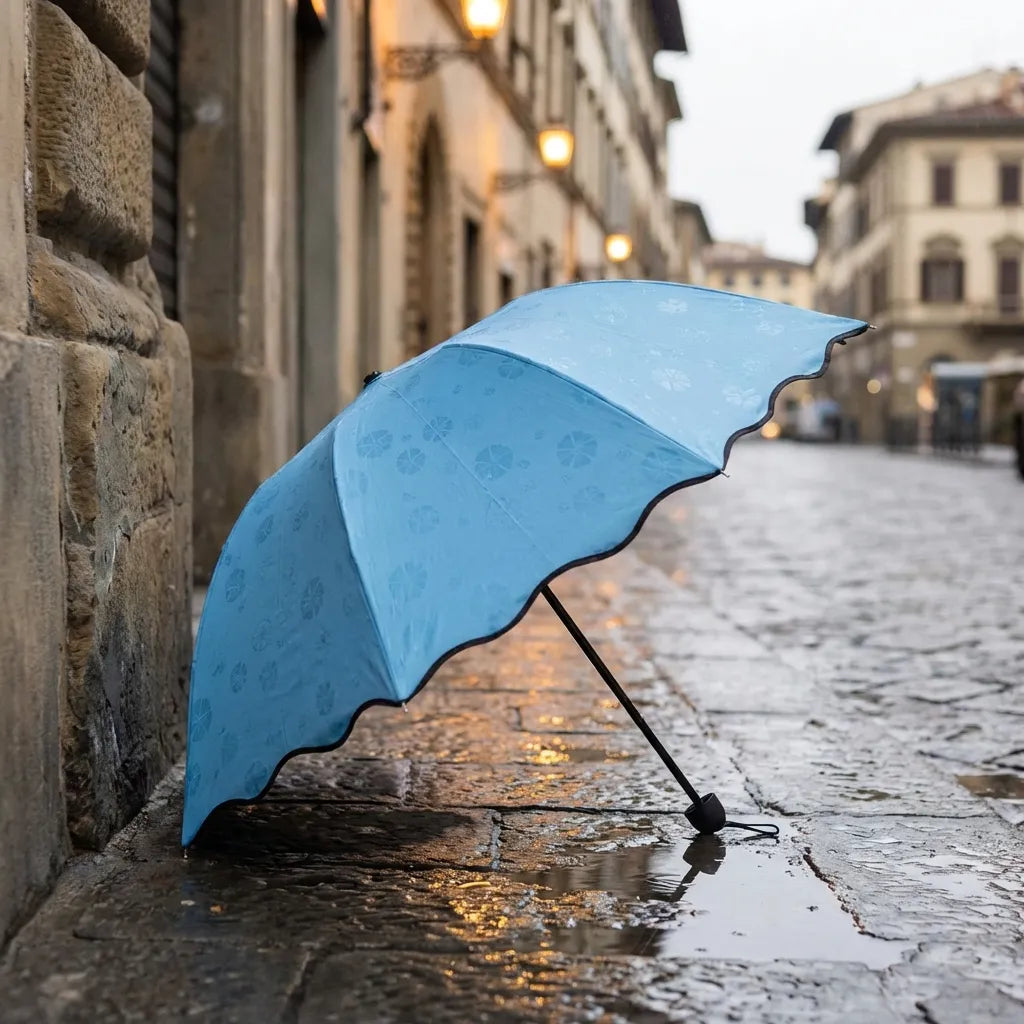 Blue umbrella with flower pattern and black underside trim, standing open on wet stones