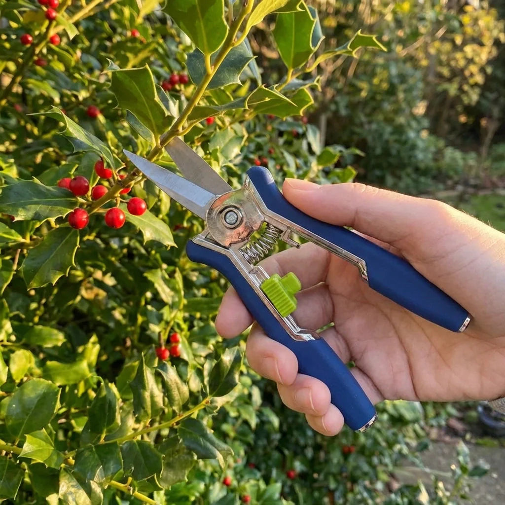Hand holding micro garden pruning snip scissors; blue grips, silver blades, green latch.