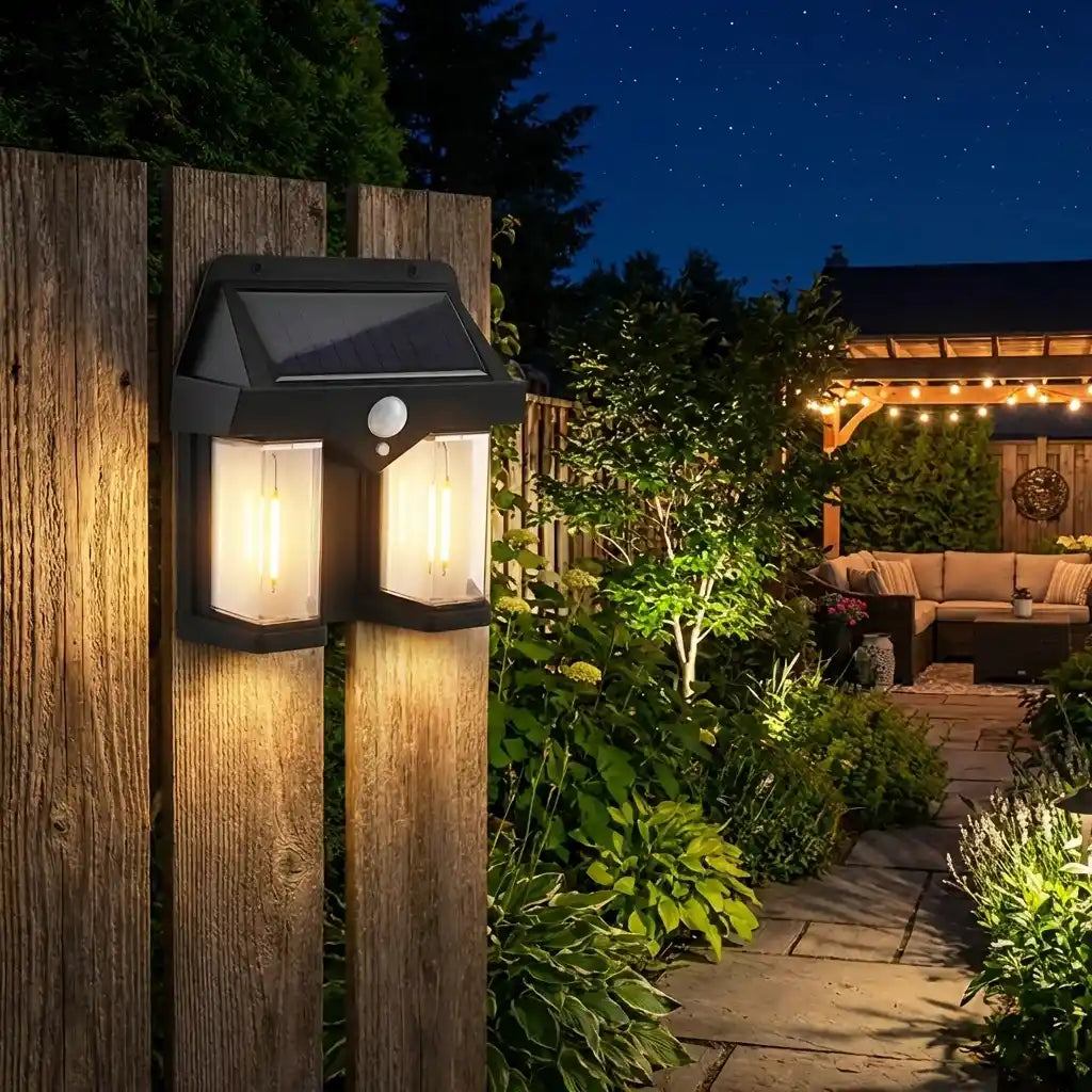 Outdoor solar wall lamp with black lantern housing and solar panel, warm light glowing on wood fence