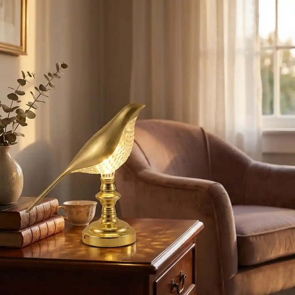 Gold sparrow-style LED table lamp with bird-shaped shade and stepped base, lit.