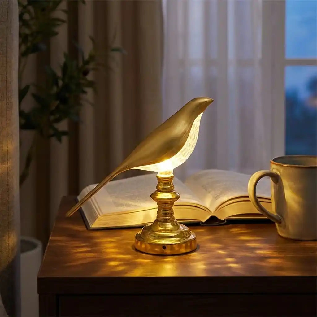 Gold sparrow-style LED table lamp with open bird-shaped shade and ribbed base, lit.