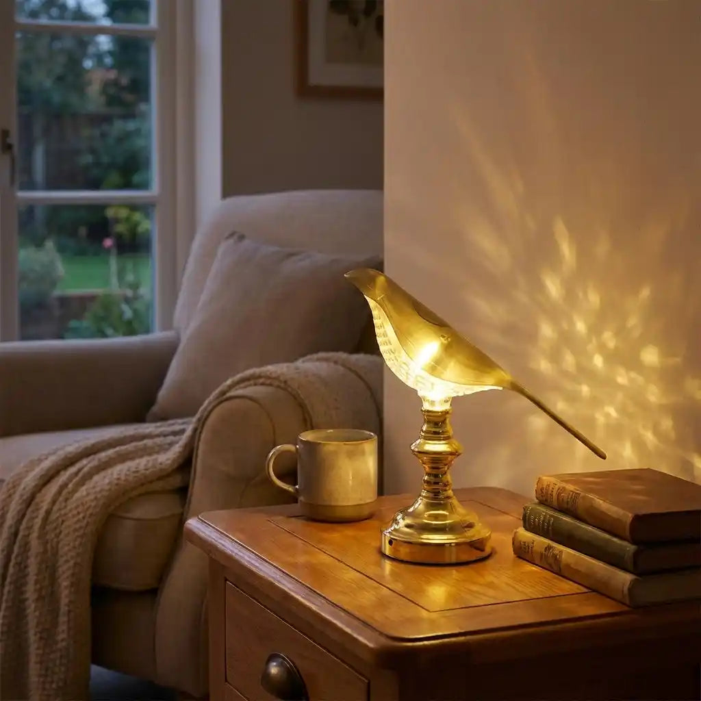 Gold sparrow LED table lamp with bird-shaped shade and glowing bulb, lit.
