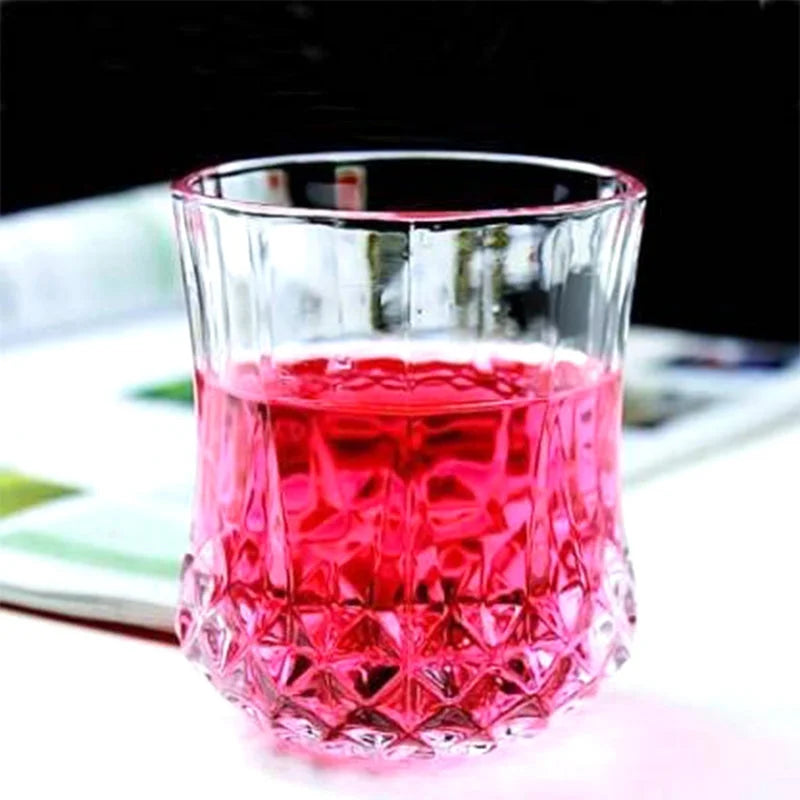 Transparent drinking glass with faceted diamond base and pink tinted drink
